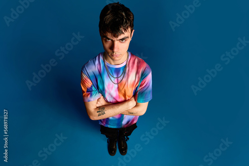 Upset young guy with folded arms in blue studio photo