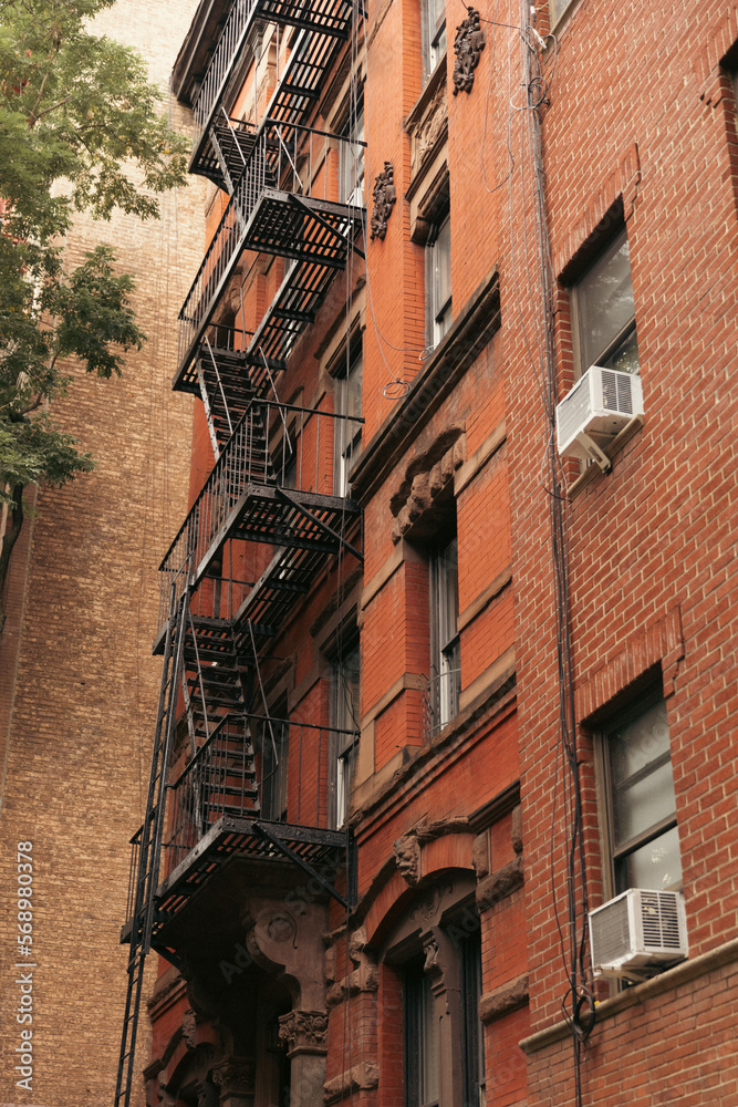 low angle view of brick building with metal balconies and fire escape ladders in New York City.
