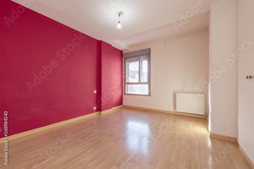 empty room with one wall painted red and the rest white, double aluminum window, white radiator and laminate floor