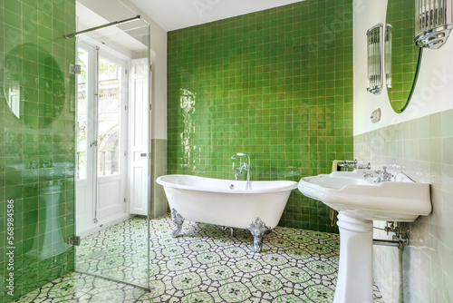 Nice bathroom decorated in vintage style with claw bathtub, hydraulic tiles on the floor and green walls