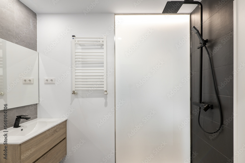 Newly renovated bathroom with black taps, square mirror, black tiles in the shower, white heated towel rail and light wood furniture with drawers Newly renovated bathroom with black taps, square mirror, black tiles in the shower, white heated towel rail and light wood furniture with drawers