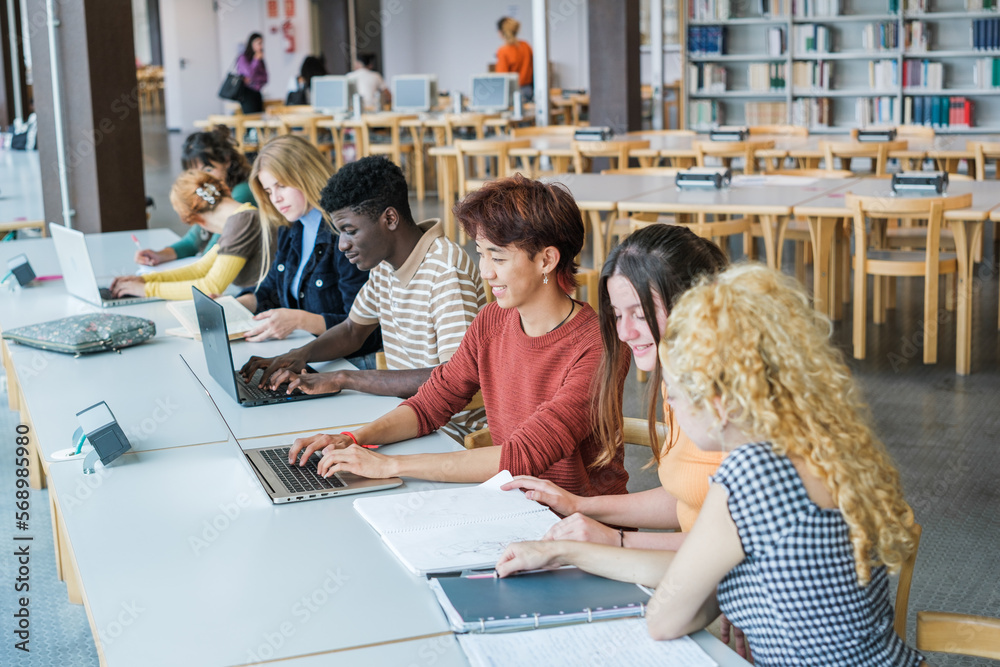 Diverse group of students in the university library sharing notes ...