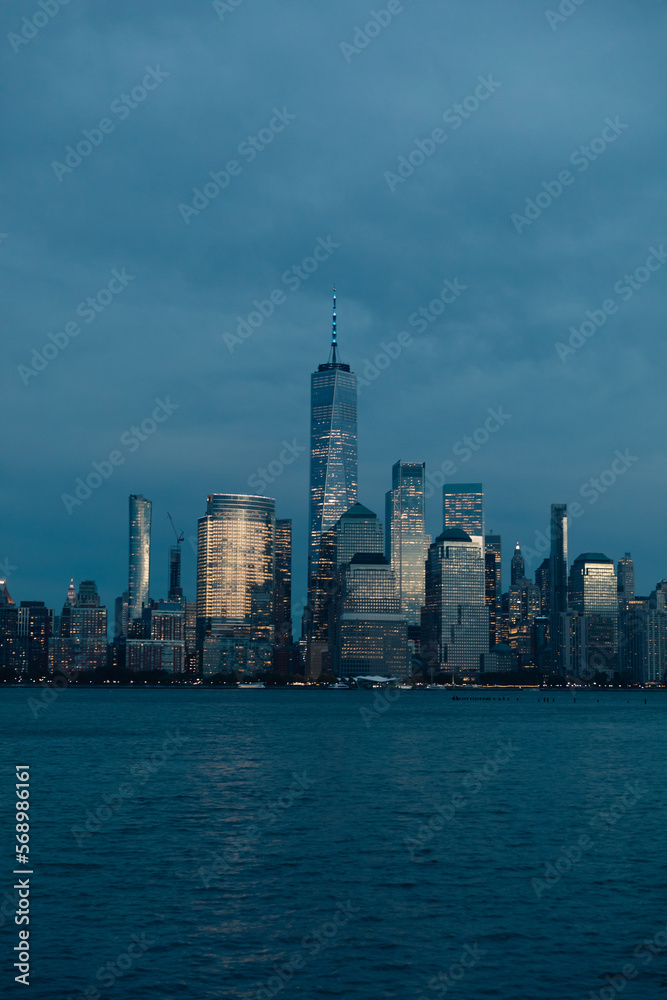New York harbor and skyline with Manhattan skyscrapers and One World Trade Center in dusk.