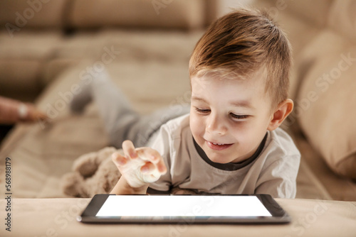 A happy little boy is using tablet for education. He is watching educational videos and smiling at the tablet.