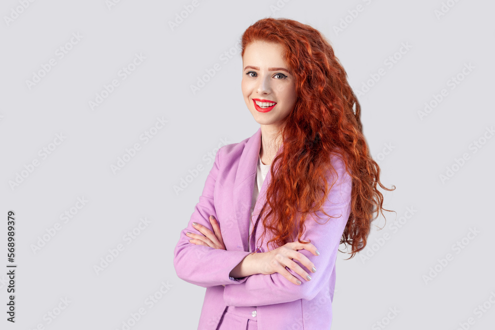 Portrait of beautiful motivated ginger woman standing with crossed hands, looking at camera with, being self-confident, wearing lilac jacket. Indoor studio shot isolated on gray background. Portrait of beautiful motivated ginger woman standing with crossed hands, looking at camera with, being self-confident, wearing lilac jacket. Indoor studio shot isolated on gray background.