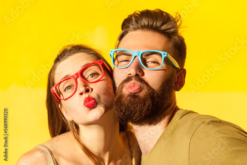 Portrait of romantic pleased loving couple standing looking at camera and sending air kiss  posing with pout lips  being on date. Indoor studio shot isolated on yellow background.