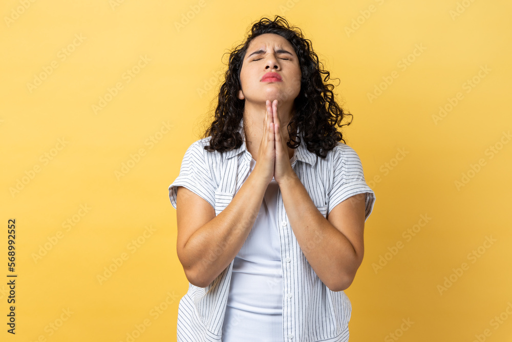 Portrait of woman with dark wavy hair standing praying up heartily, feeling guilty, pleading begging help from heaven, asking apology. Indoor studio shot isolated on yellow background. Portrait of woman with dark wavy hair standing praying up heartily, feeling guilty, pleading begging help from heaven, asking apology. Indoor studio shot isolated on yellow background.