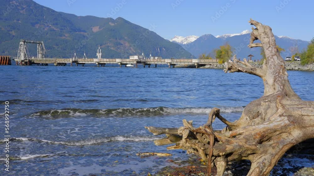 Establishing shot of ocean beach with rocks, pebbles and wood logs in slow motion at summer day in Vancouver, Canada, North America. Day time on September 2022. Still camera. ProRes 422 HQ. Establishing shot of ocean beach with rocks, pebbles and wood logs in slow motion at summer day in Vancouver, Canada, North America. Day time on September 2022. Still camera. ProRes 422 HQ.