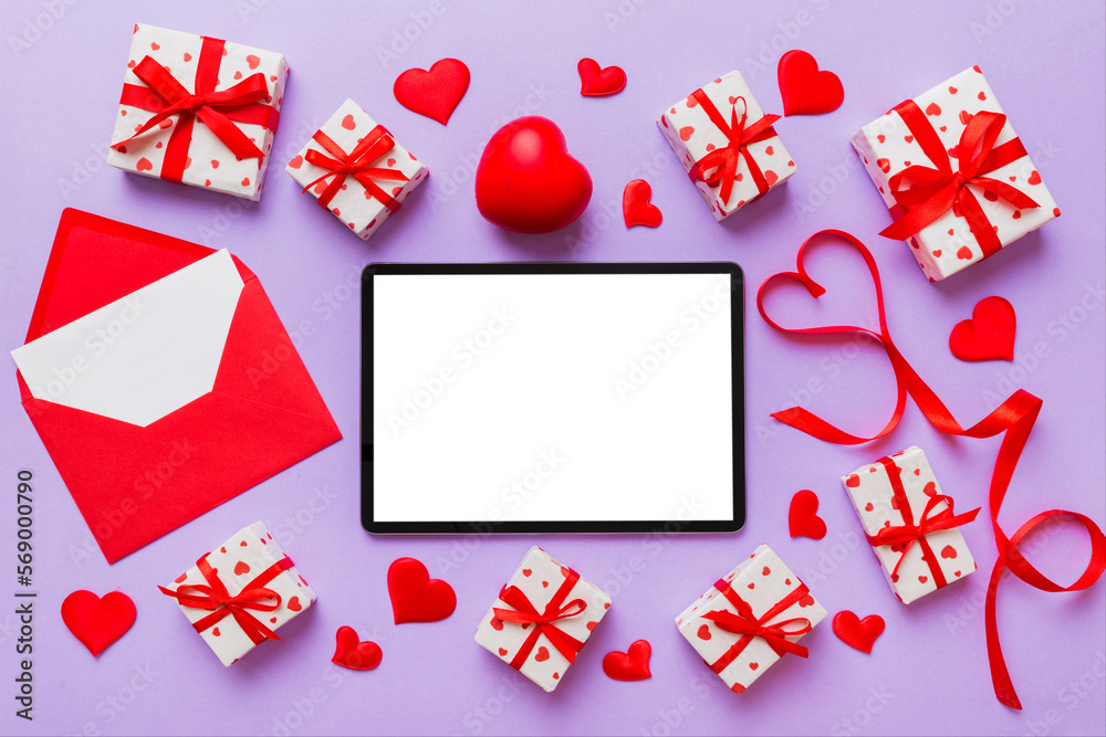 Top view of digital tablet with gift boxes and hearts on colorful background. Tablet with black screen with Holiday decorations gift box top view