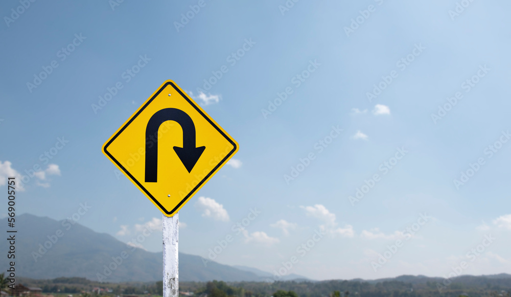 Traffic sign: Right U-turn sign on cement pole beside the rural road with white cloudy bluesky and mountains background, copy space.	