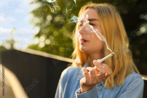 Young woman smoking cigarette outdoors, focus on hand. Space for text