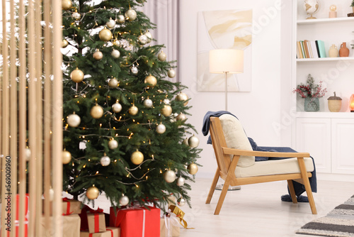 Beautiful Christmas tree with festive lights  gifts and armchair in living room. Interior design