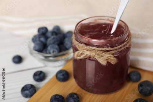 Jar of delicious blueberry jam and fresh berries on white table, closeup. Space for text