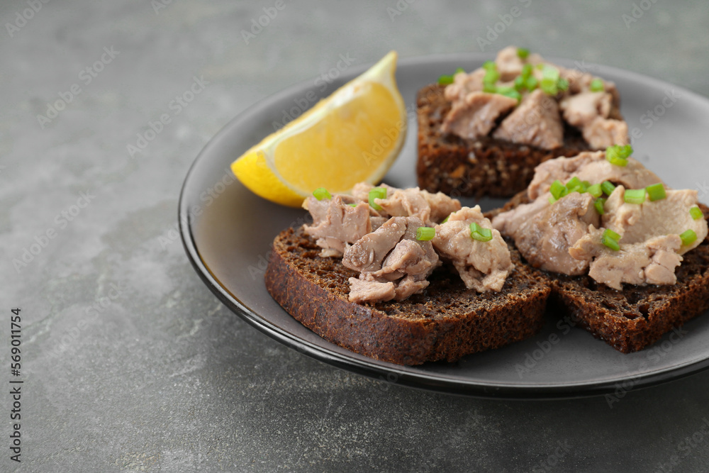 Tasty sandwiches with cod liver, lemon and green onion on light grey table Tasty sandwiches with cod liver, lemon and green onion on light grey table