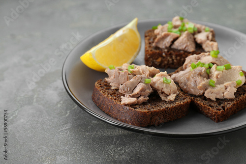 Tasty sandwiches with cod liver  lemon and green onion on light grey table