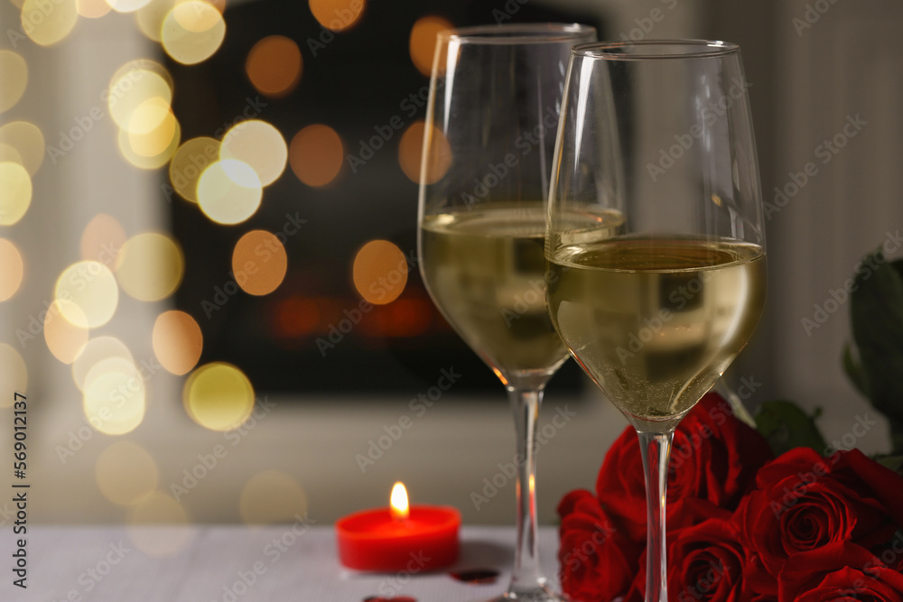 Glasses of white wine, burning candle and rose flowers on grey table indoors, space for text. Romantic atmosphere Glasses of white wine, burning candle and rose flowers on grey table indoors, space for text. Romantic atmosphere