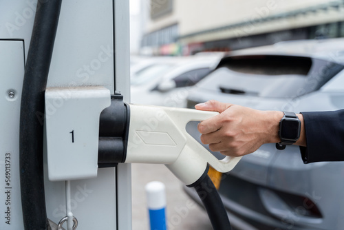 Hand of A man holding Electric Car Charging connect to Electric car on electric car charging station. Concept of green energy and reduce CO2 emission. EV car.