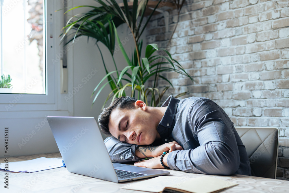 Exhausted young Caucasian male employee sleep desk at office overwork preparing report. Tired male fall asleep doze off at workplace, work late to meet deadline. Fatigue, exhaustion concept.. - obrazy, fototapety, plakaty 