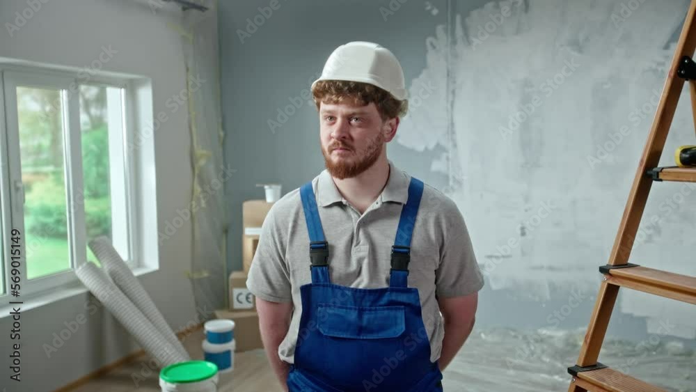 Male foreman in blue overalls and white helmet is planning renovation project and turning on an electric screwdriver. Redhead master man looking at rotating drill and thinking something. Male foreman in blue overalls and white helmet is planning renovation project and turning on an electric screwdriver. Redhead master man looking at rotating drill and thinking something.