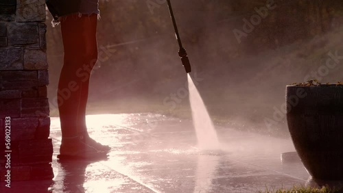 SLOW MOTION, CLOSE UP: Cleaning of outdoor surfaces with high pressure washer. Female person washes terrace floor with high pressure cleaner on a sunny day. Use of powerful water jet in golden light. photo
