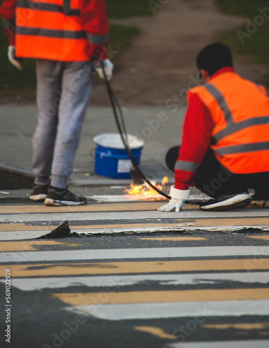 Process of making new road surface markings with a line striping machine, workers improve city infrastructure, demarcation marking of pedestrian crossing with hot melted paint on asphalt pavement
