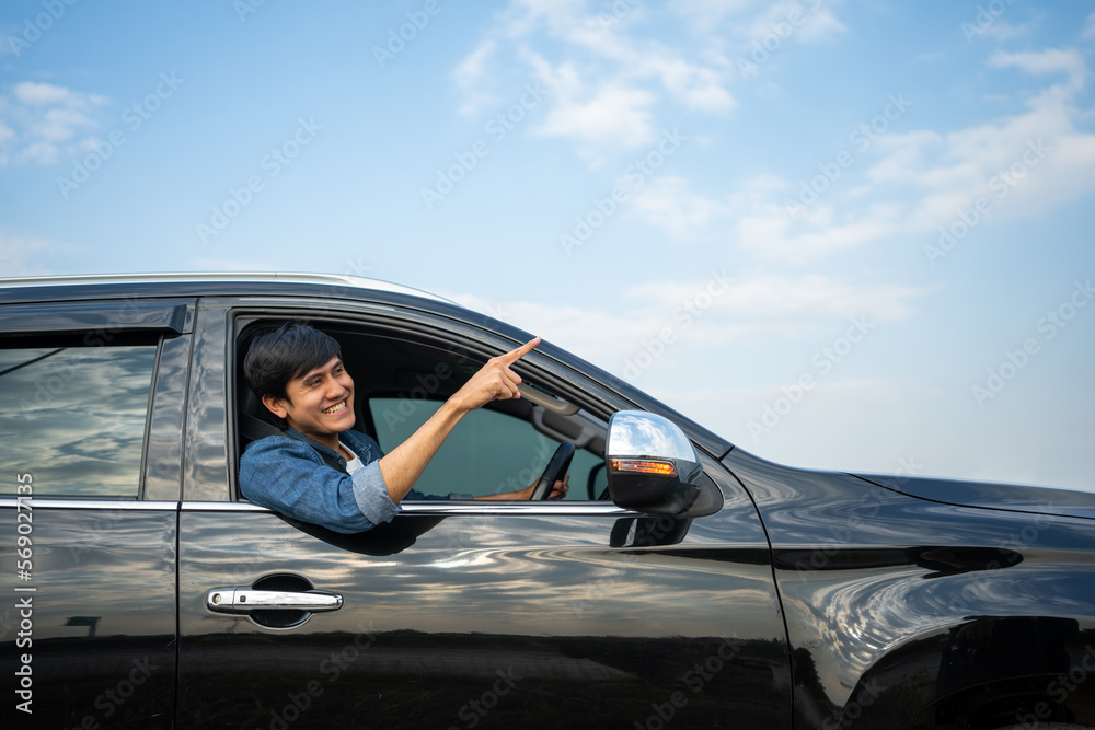 A young Asian man drives a car on a clear day. With beautiful blue sky. He smiling driving to travel by car. Sticking her head outta the windshield A young Asian man drives a car on a clear day. With beautiful blue sky. He smiling driving to travel by car. Sticking her head outta the windshield