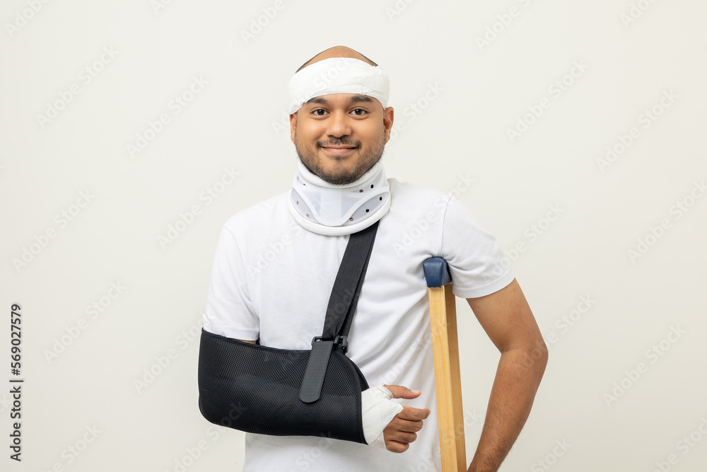 Happy young asian man broken arm and leg on isolated. Man put on plaster cast splint with walking sticks crutches. Patient wearing sling support arm with neck collar. life insurance and accident Happy young asian man broken arm and leg on isolated. Man put on plaster cast splint with walking sticks crutches. Patient wearing sling support arm with neck collar. life insurance and accident