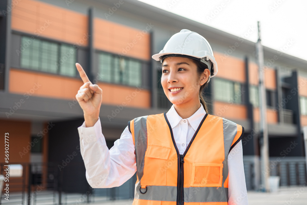 Confident engineer woman standing at modern home building construction. Architect with white safety helmet at construction site. Mechanic service factory Professional work job occupation in uniform.