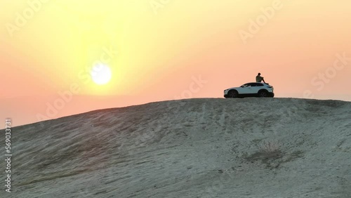 Man sits on a desert hill overlooking a sunrise in ontop of a Mazda car; Israel in the Judean Desert looking out to Jordan.