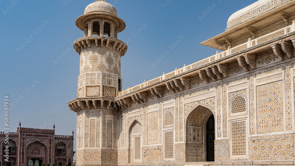 Fragment of the ancient  tomb of Itmad-Ud-Daulah. The white marble walls are decorated with ornaments, lattices, patterns, inlays of precious stones. A minaret  against the blue sky. India. Agra