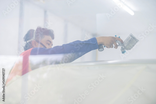 Asian auto mechanic wearing protective suit and respirator paints car body bumpers in paint room,spraying cars in paint room