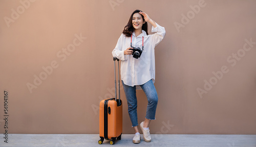 Portrait of young beautiful asian woman traveler standing hold camera suitcase full body on holiday vacation summer. Happy cheerful asian girl in summer. Korean University woman fashion lifestyle.