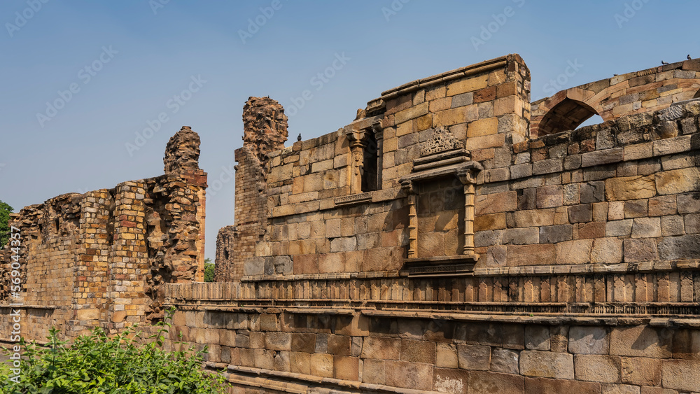 Ruins of the Qutub Minar temple complex. Dilapidated walls of red sandstone brick against the blue sky. Preserved carved ornaments are visible on the weathered surface. India. Delhi Ruins of the Qutub Minar temple complex. Dilapidated walls of red sandstone brick against the blue sky. Preserved carved ornaments are visible on the weathered surface. India. Delhi