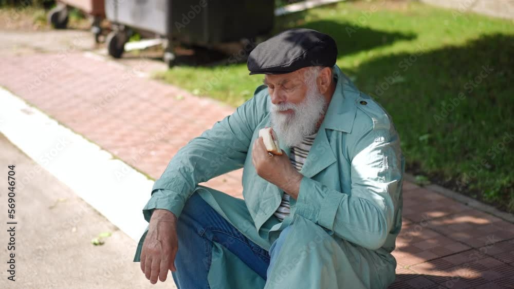 Sad homeless old man eating sandwich in slow motion sitting on curb at