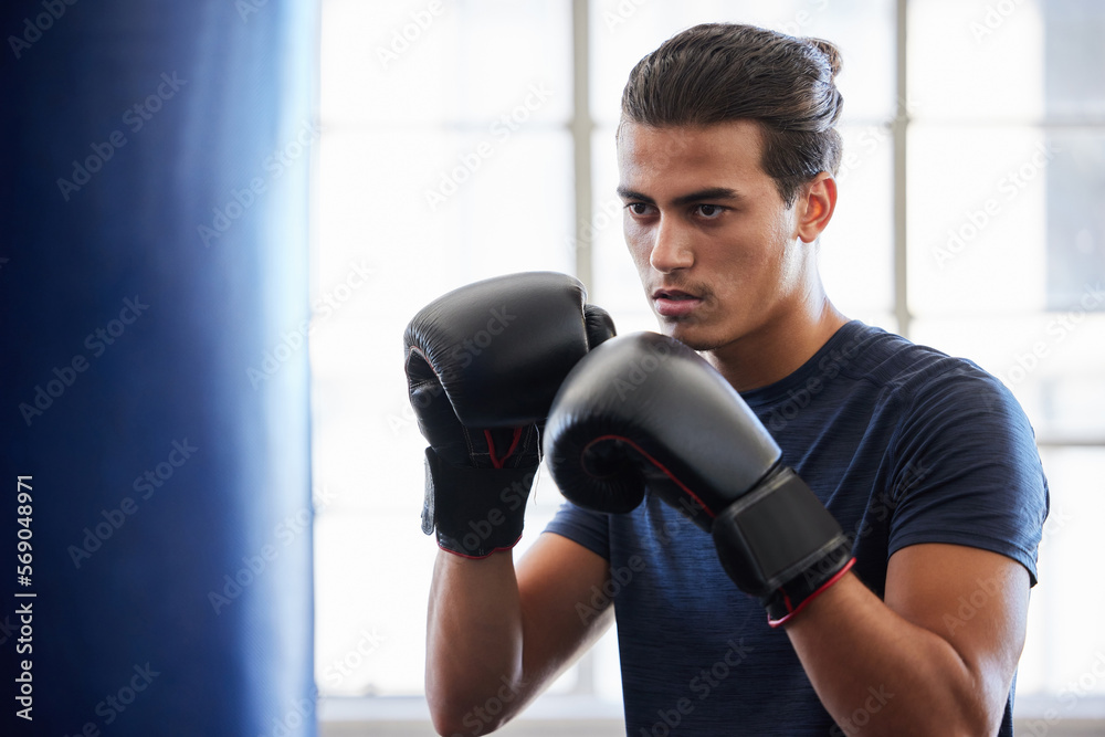 Man, boxing and fitness in gym exercise for power, performance and cardio against a window background. Boxer, fighter and athletic male training on punching bag at sports center, serious and tough