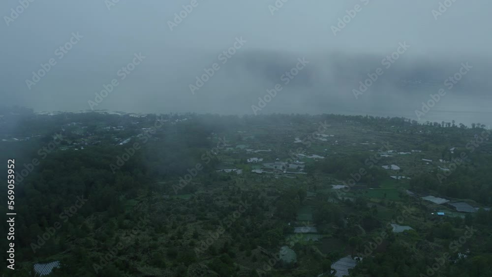 Early morning grey mood scenery, clouds close the sky, mist and fog spread on the ground. Flying in the clouds in rainy weather near lake with small asian village. Moody cinematic cold colors Early morning grey mood scenery, clouds close the sky, mist and fog spread on the ground. Flying in the clouds in rainy weather near lake with small asian village. Moody cinematic cold colors