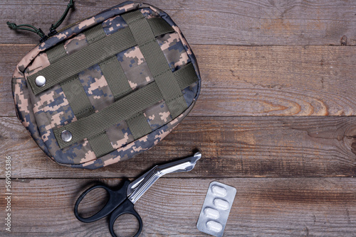 Military first aid kit in camouflage color close-up on a wooden background. First aid for wounds and injuries. Medical instruments and pain pills photo