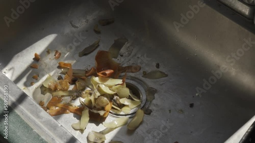 Man is disposing of the peel of carrots and potatoes from the sink on sunny day photo