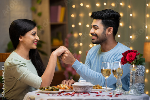 young man proposing to girlfriend by holding hands while arranging candlelight dinner - concept of love or emotion, valentine day and romantic couple photo