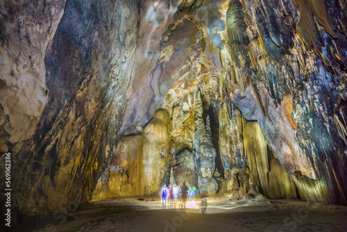 Limestone formations on the walls and roof of a huge underground cavern with people walking through at Phong Nha in Vietnam