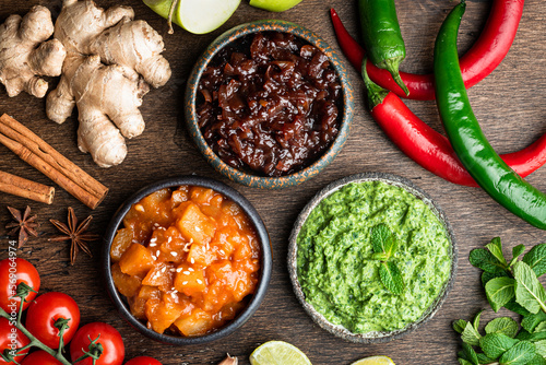 Indian chutney set in bowls on wooden background, top view photo