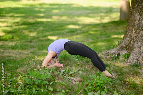 Middle-aged woman doing yoga outdoors in the park in upward-facing two- legged staff Pose.Full length.The concept of stretching, pilates, healthy lifestyle. Improves posture by increasing flexibility.