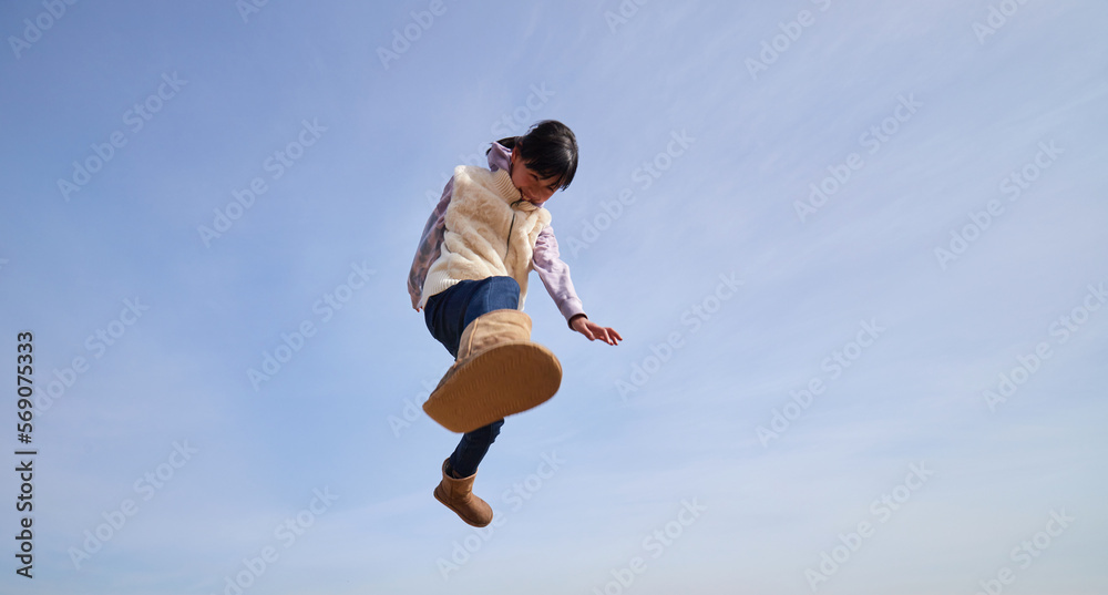 冬の青空と元気で空にジャンプしている小学生の女の子の様子
