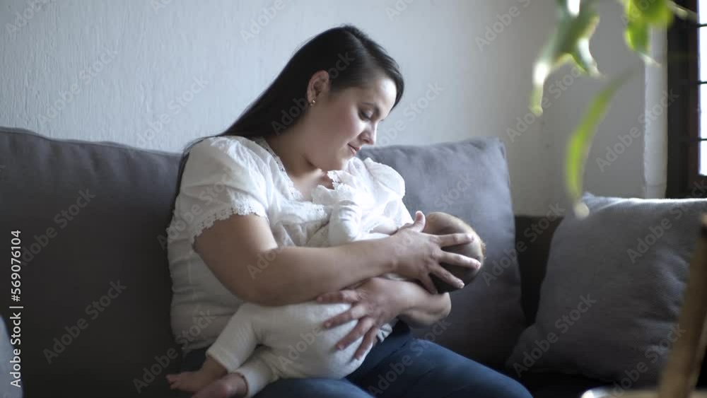 Mamá latina sentada alimentando a su bebe con el pecho realizando lactancia materna y viendo a su hija succionar.