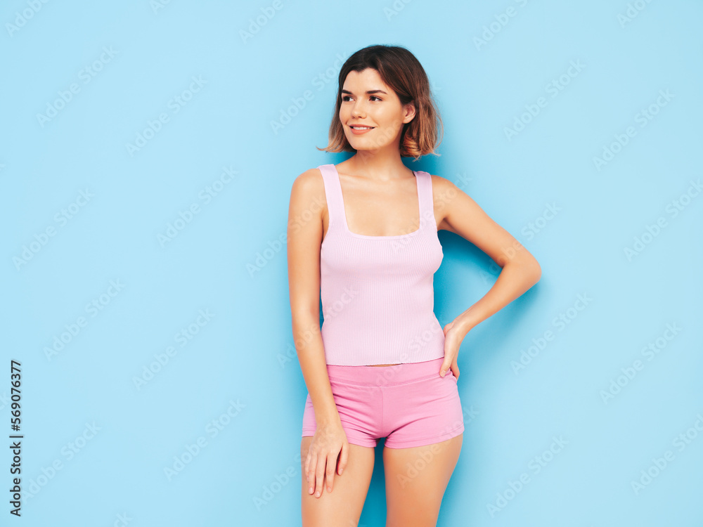 Portrait of young beautiful smiling female in trendy summer shorts clothes. Carefree woman posing near blue wall in studio. Sexy positive model having fun indoors. Cheerful and happy Portrait of young beautiful smiling female in trendy summer shorts clothes. Carefree woman posing near blue wall in studio. Sexy positive model having fun indoors. Cheerful and happy