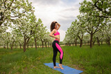 Athletic young woman in pink suit posing on blue rug in blooming garden