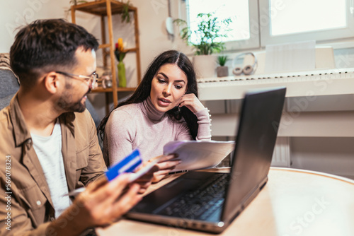 Young couple paying bills together, customers paying by credit card online, sitting in cozy living room at home