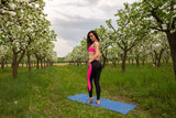 Athletic young woman in pink suit posing on blue rug in blooming garden