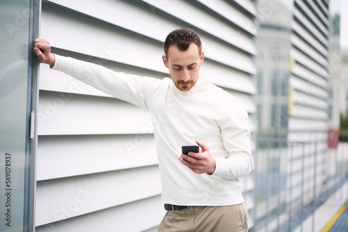 Serious stylish guy using mobile banking app while standing at street. Bearded businessman shopping online outdoors © Maria Vitkovska