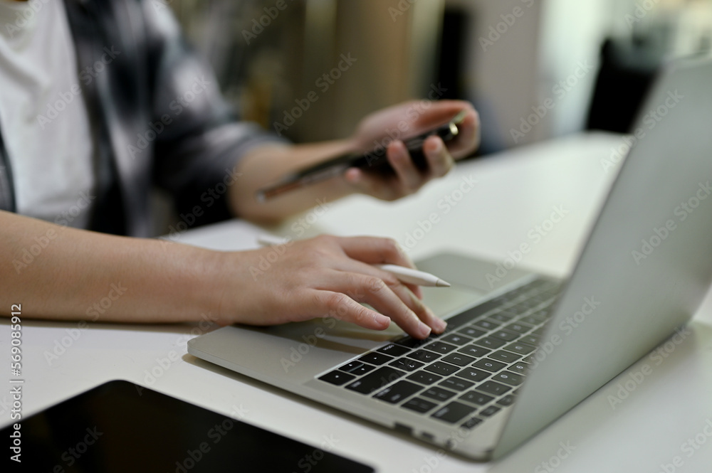 Close-up image of a businesswoman using her smartphone and working on her project on laptop Close-up image of a businesswoman using her smartphone and working on her project on laptop